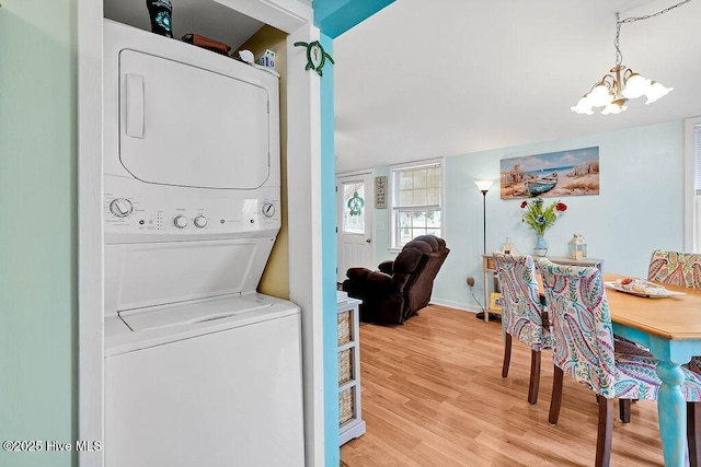 laundry area with an inviting chandelier, light wood-type flooring, and stacked washer / dryer