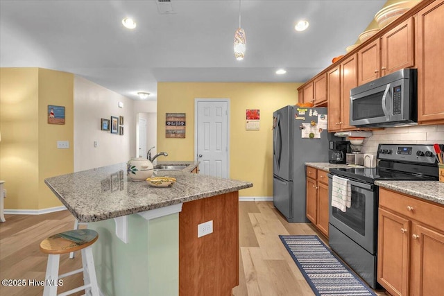 kitchen featuring stainless steel appliances, an island with sink, sink, and light stone counters