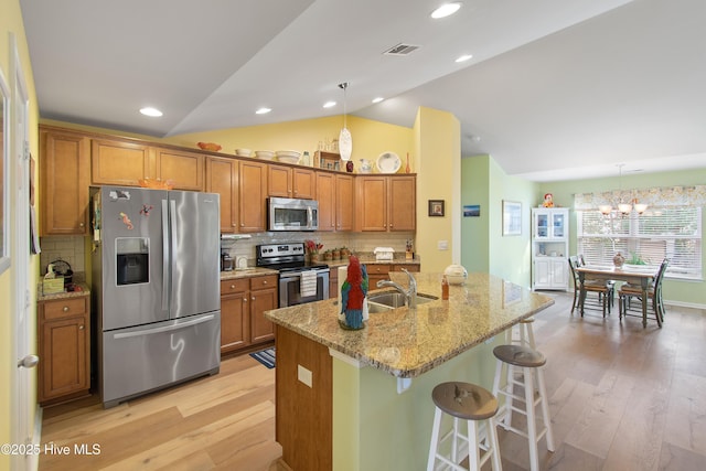 kitchen with a breakfast bar, sink, hanging light fixtures, appliances with stainless steel finishes, and light stone countertops