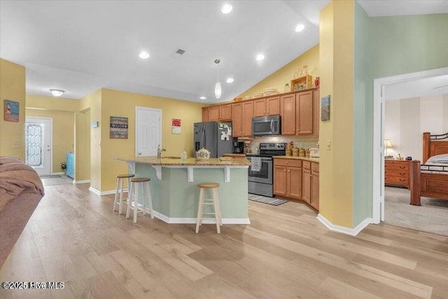 kitchen with appliances with stainless steel finishes, high vaulted ceiling, a kitchen breakfast bar, a center island with sink, and light wood-type flooring