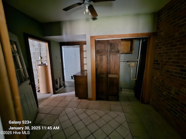 interior space with ceiling fan, brick wall, light tile patterned floors, and gas water heater