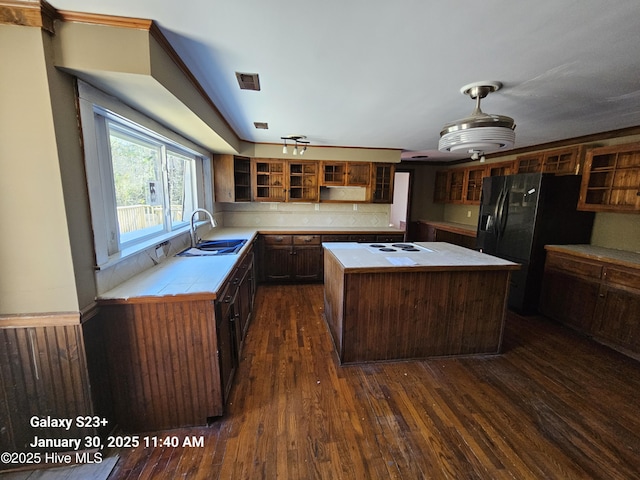 kitchen with cooktop, sink, black fridge, dark hardwood / wood-style flooring, and a kitchen island