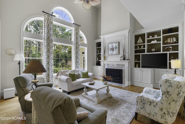 living room with a high ceiling, a high end fireplace, and light wood-type flooring