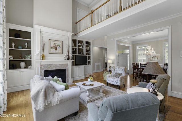 living room featuring built in features, wood-type flooring, a high ceiling, ornamental molding, and a notable chandelier