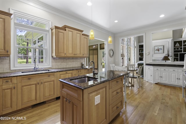 kitchen featuring decorative light fixtures, sink, dark stone counters, a kitchen island with sink, and crown molding