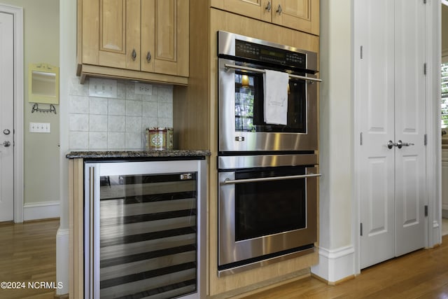 kitchen with hardwood / wood-style floors, beverage cooler, dark stone counters, decorative backsplash, and stainless steel double oven