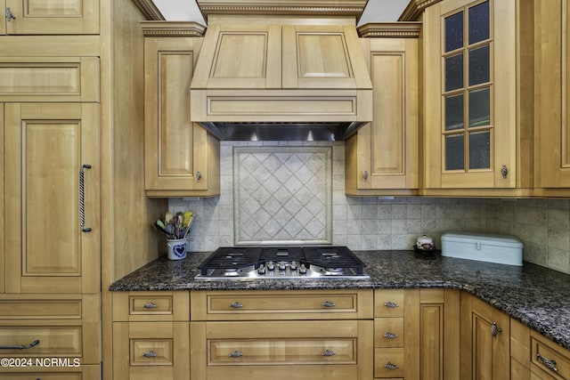 kitchen featuring stainless steel gas stovetop, premium range hood, dark stone countertops, and backsplash