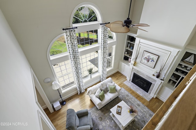 living room featuring a premium fireplace, hardwood / wood-style floors, built in features, and a high ceiling