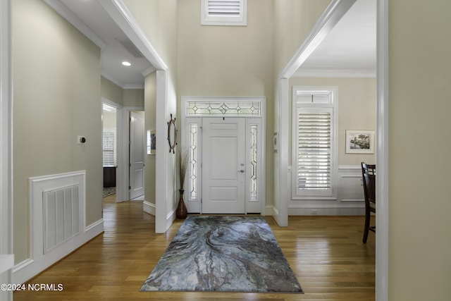 foyer with ornamental molding, wood-type flooring, and a towering ceiling