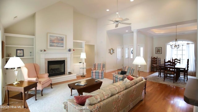 living room featuring hardwood / wood-style flooring, a tile fireplace, high vaulted ceiling, ceiling fan with notable chandelier, and ornate columns