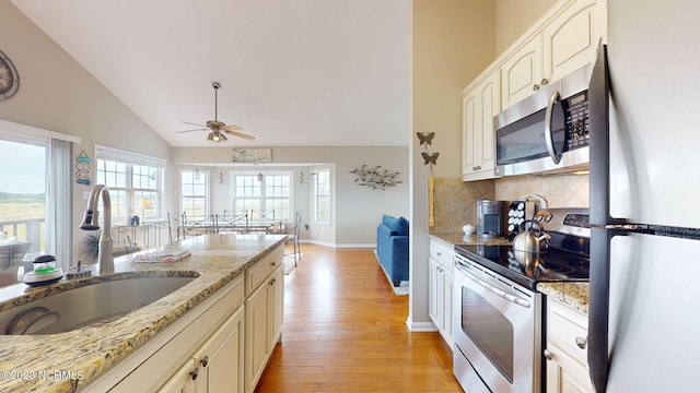 kitchen featuring sink, appliances with stainless steel finishes, light stone countertops, decorative backsplash, and light wood-type flooring