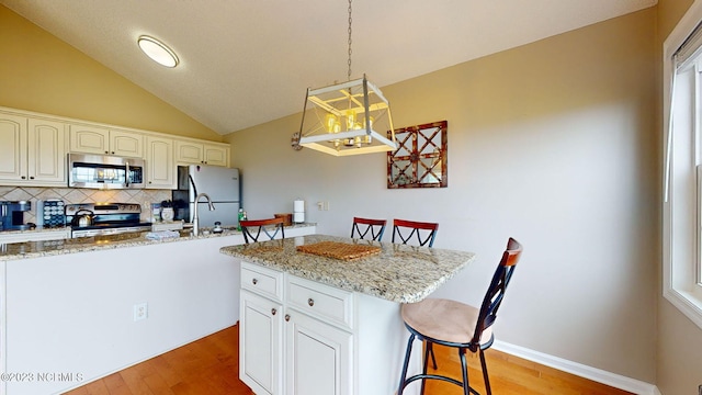 kitchen with decorative light fixtures, white cabinets, a kitchen breakfast bar, stainless steel appliances, and light stone countertops