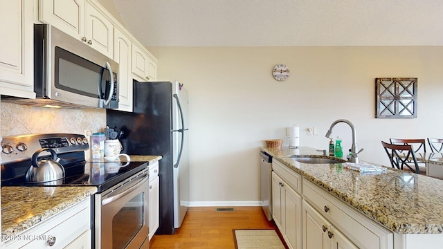 kitchen with sink, backsplash, stainless steel appliances, light stone countertops, and light wood-type flooring