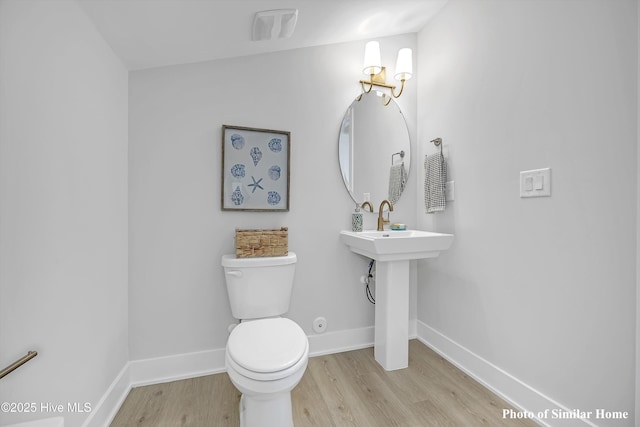 half bathroom with visible vents, baseboards, toilet, and wood finished floors