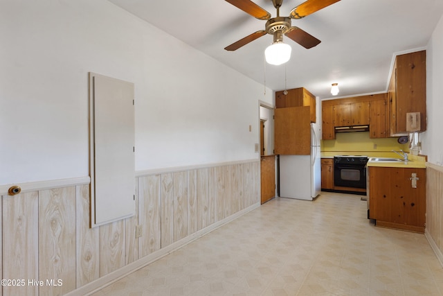 kitchen with black electric range oven, sink, ceiling fan, wood walls, and white fridge