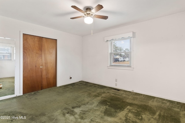 unfurnished bedroom with ceiling fan, a closet, dark carpet, and multiple windows