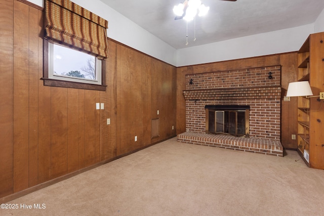 unfurnished living room with ceiling fan, wooden walls, a brick fireplace, and light carpet