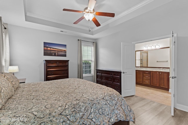 bedroom featuring crown molding, ensuite bath, a raised ceiling, ceiling fan, and light hardwood / wood-style floors