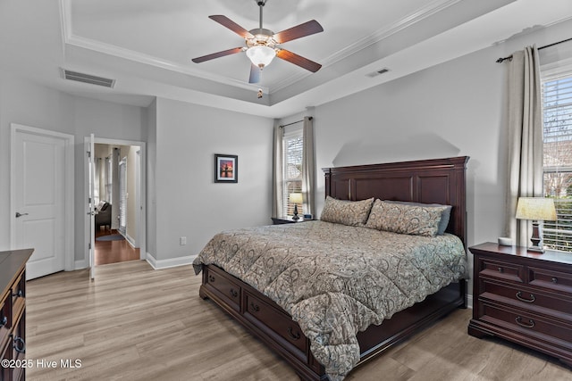 bedroom with a raised ceiling, multiple windows, and light wood-type flooring