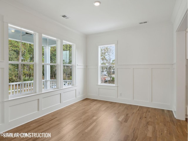 empty room with light wood finished floors, visible vents, and a decorative wall