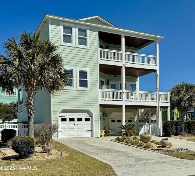 raised beach house with a balcony, an attached garage, and driveway