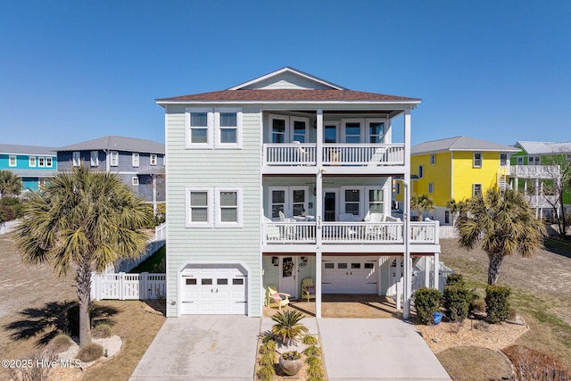 raised beach house with a balcony, an attached garage, driveway, and fence