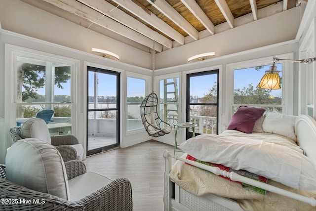 bedroom featuring beamed ceiling, a water view, hardwood / wood-style floors, and access to exterior