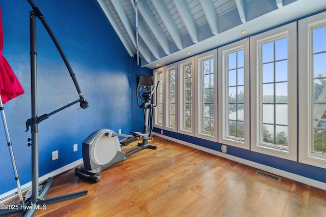 workout area with vaulted ceiling, a water view, and hardwood / wood-style floors