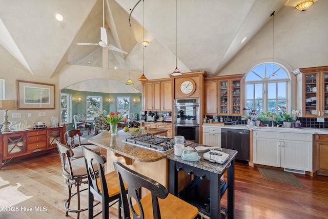 kitchen featuring decorative light fixtures, high vaulted ceiling, appliances with stainless steel finishes, light stone countertops, and light hardwood / wood-style floors