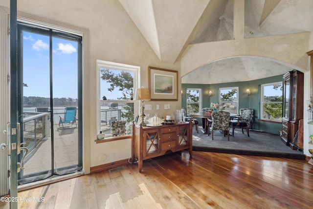 dining space featuring vaulted ceiling, wood-type flooring, and a water view