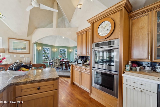 kitchen with double oven, light hardwood / wood-style floors, dark stone counters, and high vaulted ceiling