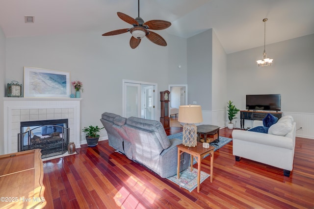 living room featuring a tiled fireplace, ceiling fan with notable chandelier, hardwood / wood-style floors, and high vaulted ceiling