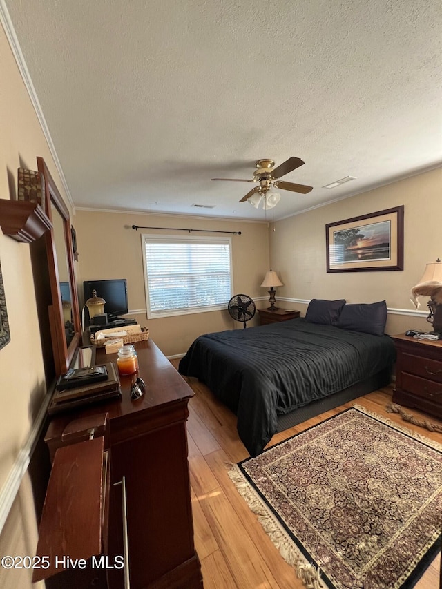 bedroom with ceiling fan, ornamental molding, light hardwood / wood-style floors, and a textured ceiling