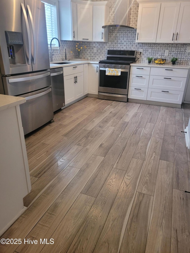 kitchen featuring wall chimney exhaust hood, sink, white cabinetry, light hardwood / wood-style flooring, and appliances with stainless steel finishes