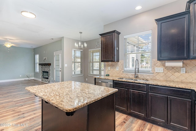 kitchen featuring a stone fireplace, sink, light hardwood / wood-style flooring, a kitchen island, and pendant lighting