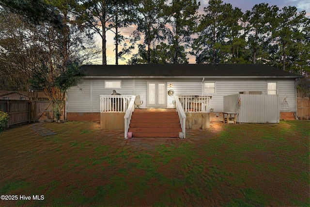 back of house at dusk featuring a deck, fence, a yard, french doors, and stairway