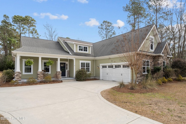 view of front of house with roof with shingles, a porch, concrete driveway, a garage, and stone siding