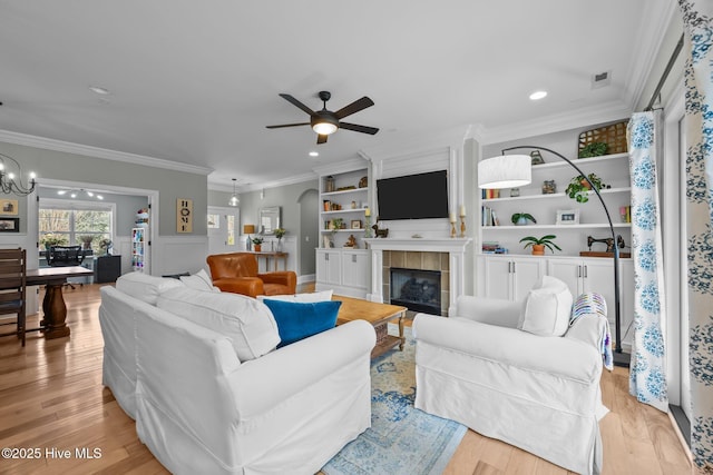 living room with a tile fireplace, ceiling fan with notable chandelier, crown molding, light wood-style floors, and recessed lighting