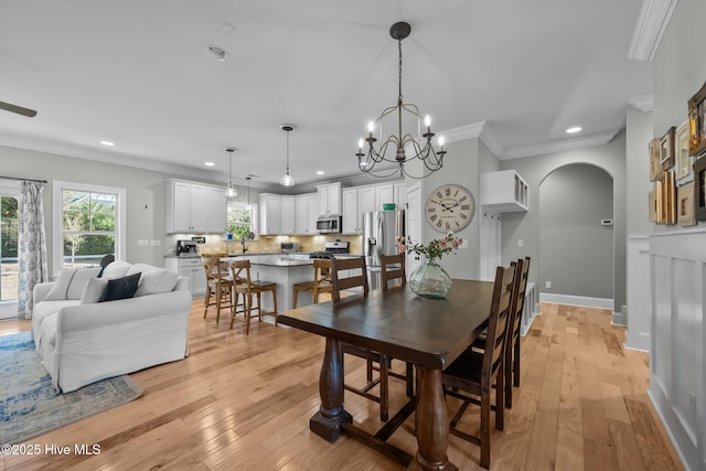 dining space with light wood-type flooring, crown molding, arched walkways, and recessed lighting