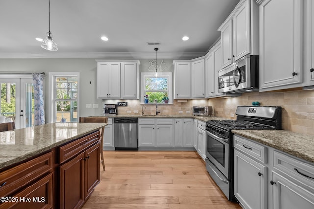 kitchen with crown molding, light wood finished floors, stainless steel appliances, visible vents, and a sink