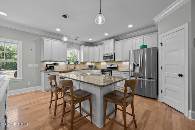 kitchen with stainless steel appliances, a breakfast bar, a sink, ornamental molding, and light wood finished floors