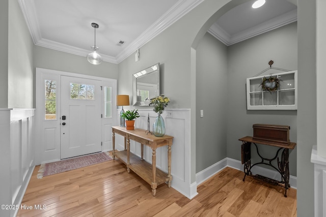 entrance foyer featuring ornamental molding, arched walkways, visible vents, and light wood-style flooring