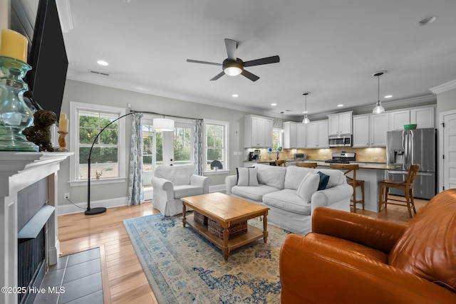 living area featuring visible vents, baseboards, light wood-style flooring, ornamental molding, and recessed lighting