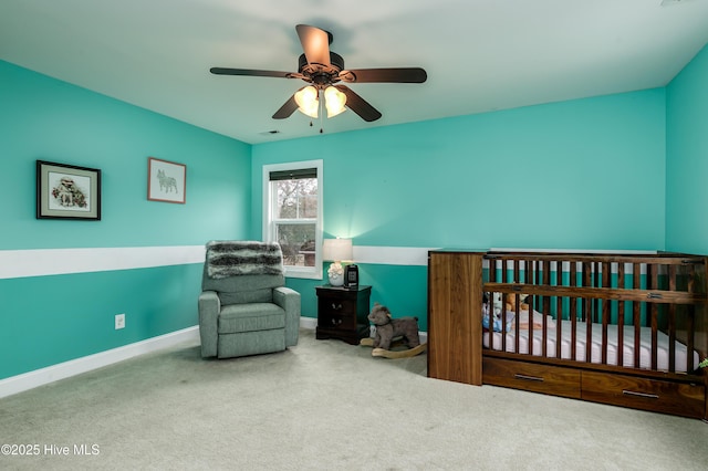 carpeted bedroom featuring ceiling fan and a crib