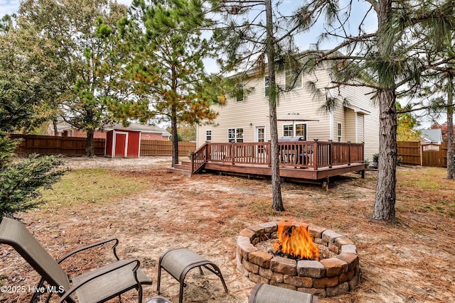 rear view of property featuring a storage shed, a wooden deck, and a fire pit