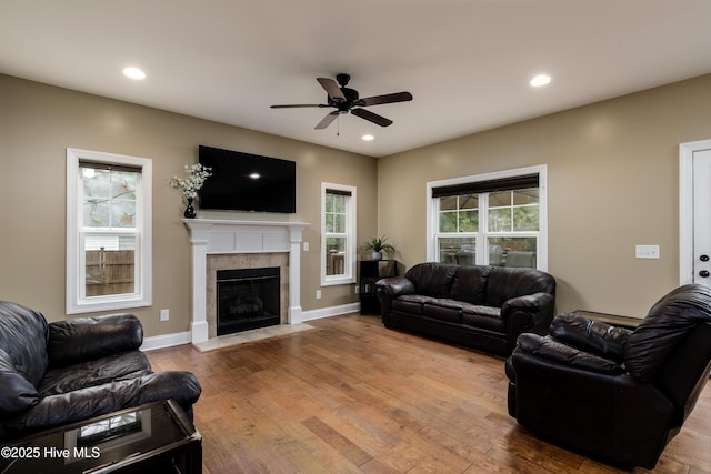 living room with a tile fireplace, wood-type flooring, a healthy amount of sunlight, and ceiling fan