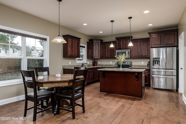 kitchen with pendant lighting, dark brown cabinets, stainless steel appliances, a center island, and a healthy amount of sunlight