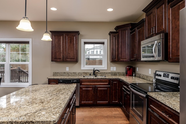 kitchen featuring appliances with stainless steel finishes, pendant lighting, sink, light stone counters, and light hardwood / wood-style floors