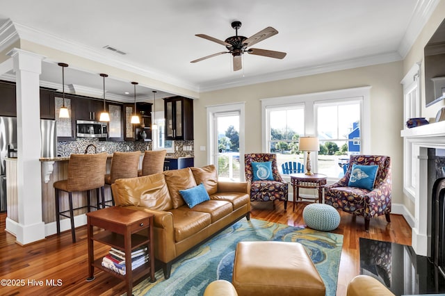 living room with crown molding, dark wood-type flooring, decorative columns, and ceiling fan