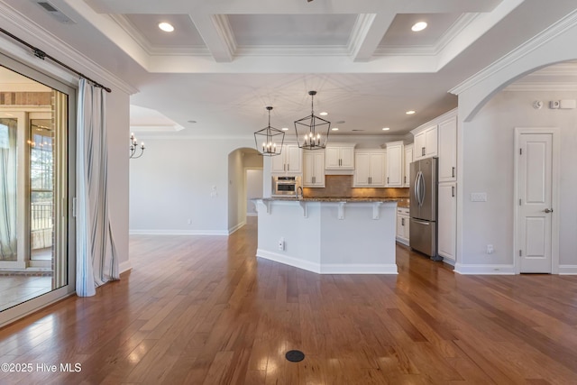 kitchen with appliances with stainless steel finishes, white cabinetry, dark stone countertops, a kitchen bar, and a center island with sink